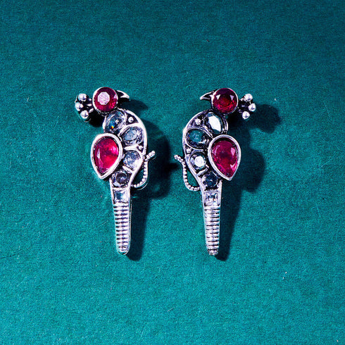 Silver peacock-shaped earrings adorned with ruby and clear gemstones, showcasing an elegant bird design with vivid red accents. From Trenzify Store.
