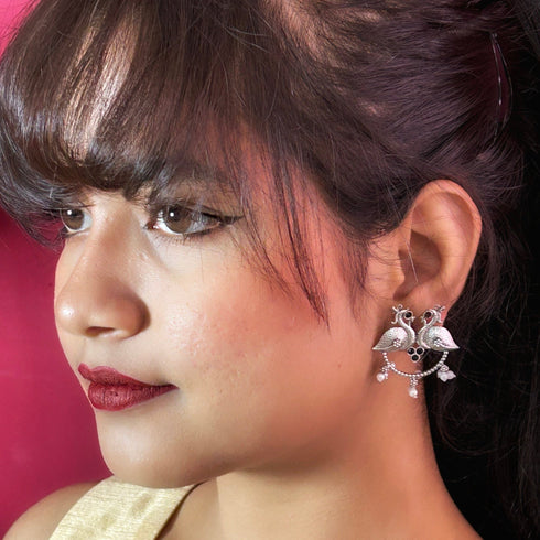 Antique-style silver peacock earrings adorned with black stones and white pearl danglers, combining tradition with bold elegance. Trenzify Store