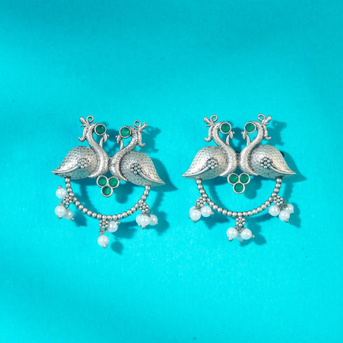 Artistic peacock earrings in oxidized silver with green stone embellishments and hanging pearl details, ideal for ethnic and fusion looks. Trenzify Store