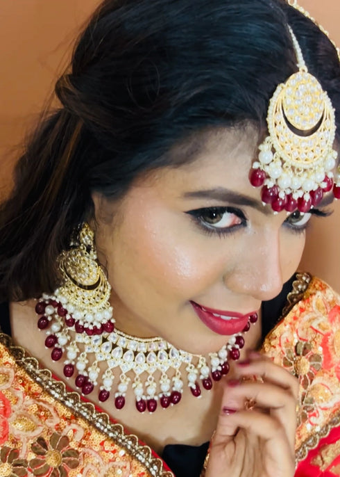 Model wearing complete kundan bridal jewelry set featuring necklace, earrings, maang tikka and passa with red beads and pearls - Trenzify Store