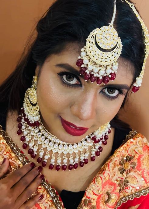 Model wearing complete kundan bridal jewelry set featuring necklace, earrings, maang tikka and passa with red beads and pearls - Trenzify Store