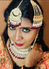 Model wearing complete kundan bridal jewelry set featuring necklace, earrings, maang tikka and passa with red beads and pearls - Trenzify Store