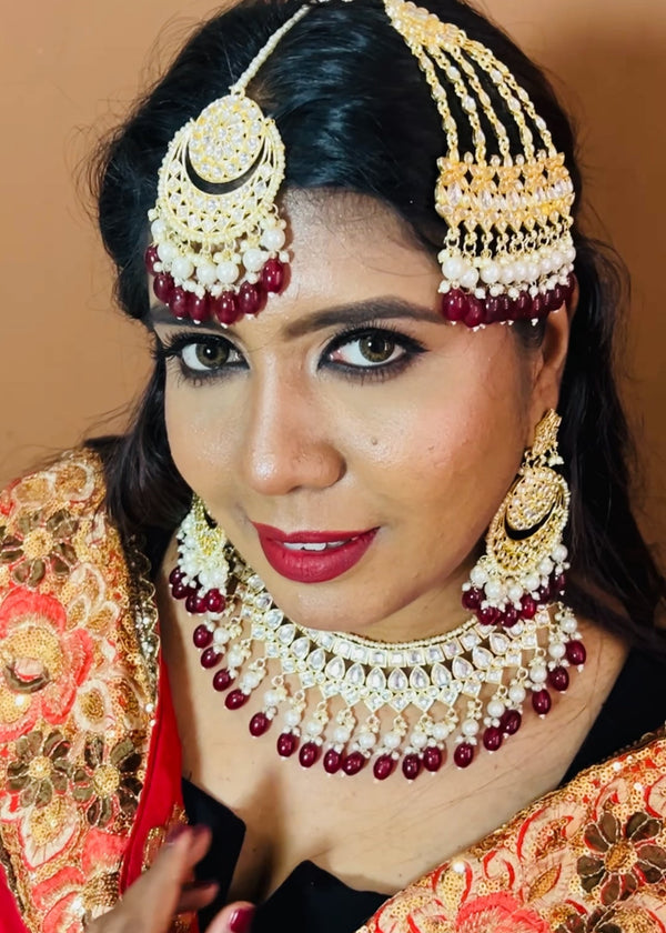Model wearing complete kundan bridal jewelry set featuring necklace, earrings, maang tikka and passa with red beads and pearls - Trenzify Store