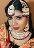 Model wearing complete kundan bridal jewelry set featuring necklace, earrings, maang tikka and passa with red beads and pearls - Trenzify Store