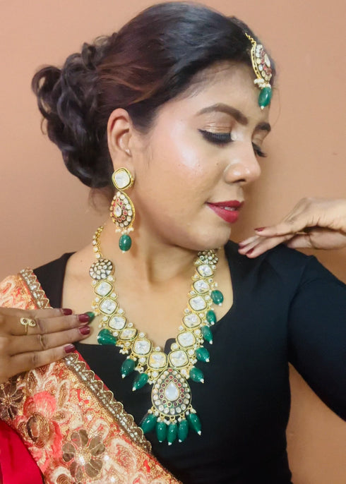 Model wearing gold plated Kundan necklace set with green stones, red enamel accents, pearls and matching earrings and maang tikka – traditional bridal jewelry from Trenzify Store.