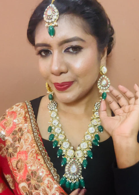 Model wearing gold plated Kundan necklace set with green stones, red enamel accents, pearls and matching earrings and maang tikka – traditional bridal jewelry from Trenzify Store.