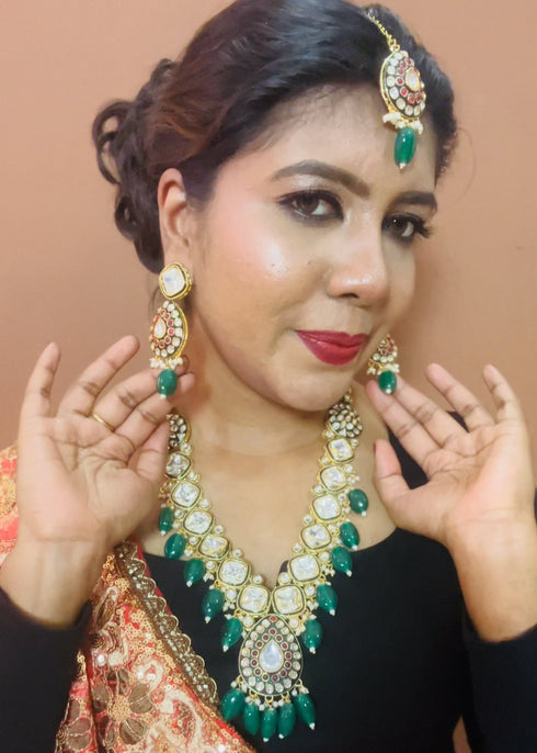 Model wearing gold plated Kundan necklace set with green stones, red enamel accents, pearls and matching earrings and maang tikka – traditional bridal jewelry from Trenzify Store.
