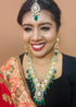 Model wearing gold plated Kundan necklace set with green stones, red enamel accents, pearls and matching earrings and maang tikka – traditional bridal jewelry from Trenzify Store.