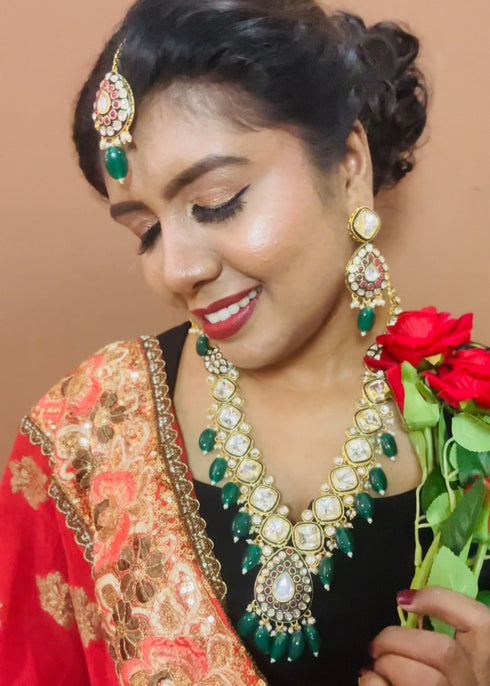 Model wearing gold plated Kundan necklace set with green stones, red enamel accents, pearls and matching earrings and maang tikka – traditional bridal jewelry from Trenzify Store.