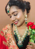 Model wearing gold plated Kundan necklace set with green stones, red enamel accents, pearls and matching earrings and maang tikka – traditional bridal jewelry from Trenzify Store.