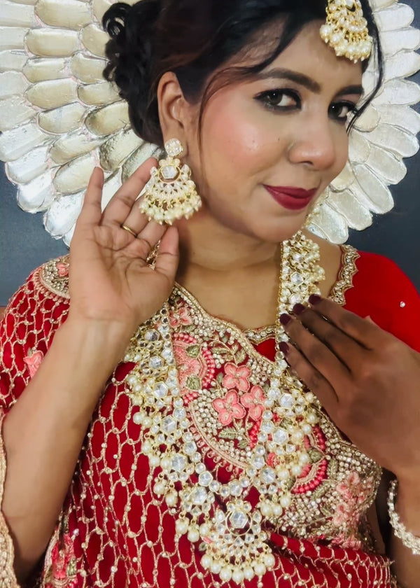 Indian bride wearing elegant Kundan bridal jewelry set with long necklace, matching earrings , and maang tikka embellished with pearls and stones - Trenzify Store.