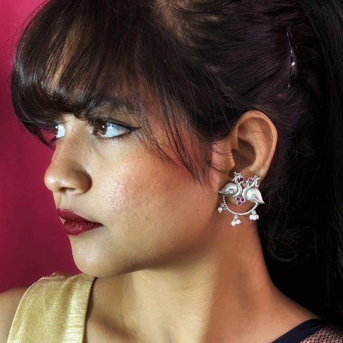 Elegant oxidized silver earrings featuring twin peacocks with ruby red stone accents and delicate pearl drops, perfect for traditional or festive occasions. Trenzify Store